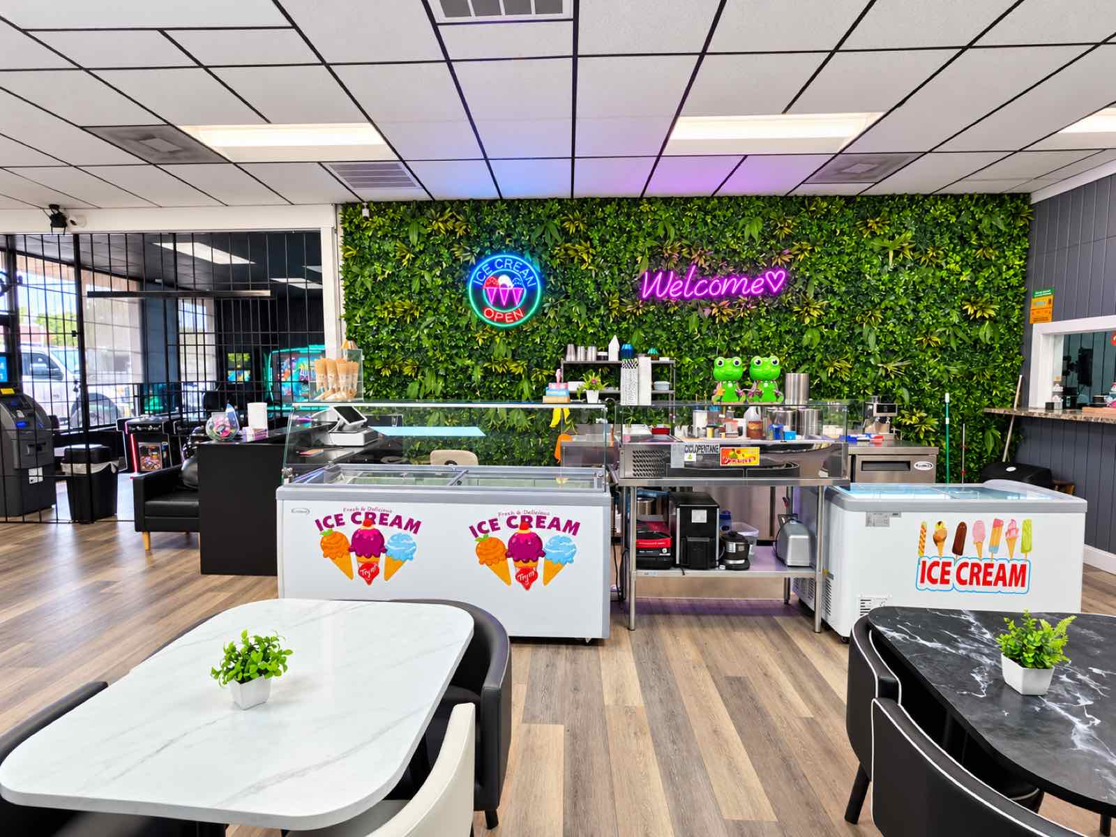 Zona de helados con congeladores, pared verde con letrero de neón Welcome y mesas